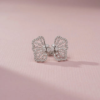 Front view of butterfly diamond stud earrings in white gold, featuring intricate openwork wings adorned with sparkling diamonds. Displayed on a soft pink backdrop, the design exudes elegance.