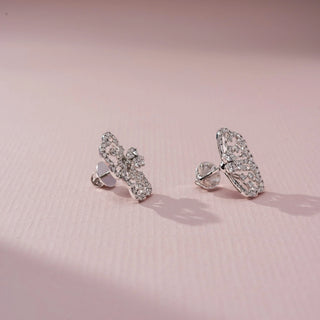 Side view of butterfly diamond stud earrings in white gold, featuring intricate openwork wings adorned with sparkling diamonds. Displayed on a soft pink backdrop, the profile highlights delicate craftsmanship.