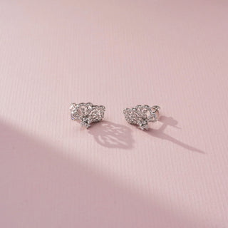 Angled view of butterfly diamond stud earrings in white gold, featuring intricate openwork wings adorned with sparkling diamonds. Displayed on a soft pink backdrop, the delicate design radiates elegance.
