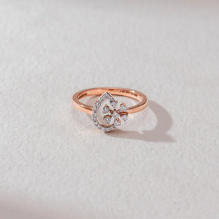 Top view of floral diamond ring in rose gold, featuring round lab-grown diamonds in a blooming cluster within a teardrop frame lined with diamonds. Set on a soft neutral surface, it reflects delicate sparkle.