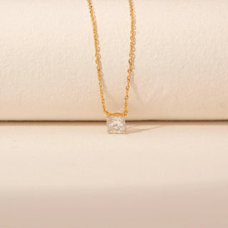 Close-up view of a 14KT yellow gold chain necklace featuring a square cushion-cut diamond pendant on a beige backdrop.