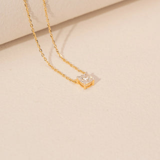 Angled view of a 14KT yellow gold chain necklace featuring a square cushion-cut diamond pendant on a beige backdrop.