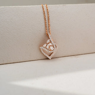 Close-up of a rose gold pendant necklace featuring a diamond-studded open teardrop frame and floral diamond centerpiece, showcased against a soft cream background.