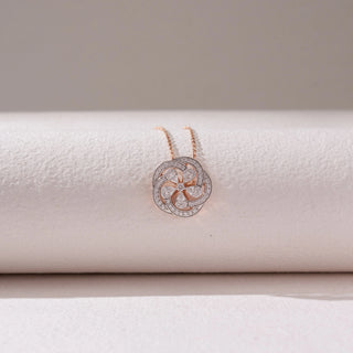 Front view of a floral diamond pendant necklace in rose gold, featuring petal-shaped diamonds within a pavé circular frame. Captured against a soft beige backdrop, the design reflects graceful sparkle and elegance.
