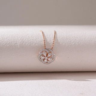 Top view of a floral diamond pendant necklace in rose gold, featuring petal-shaped diamonds within a pavé circular frame. Captured against a soft beige backdrop, the design reflects graceful sparkle and elegance.
