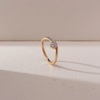 Angled side view of a yellow gold solitaire ring featuring a round lab-grown diamond and pavé-set accent diamonds along one shoulder. Captured against a beige backdrop, the slender band design highlights graceful brilliance.