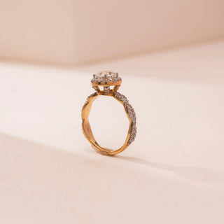 Side view of Reia’s 14 KT Yellow Gold Eternal Halo Ring. The round diamond and its halo are held in an elevated setting on a diamond-studded infinity band against a soft pink surface.