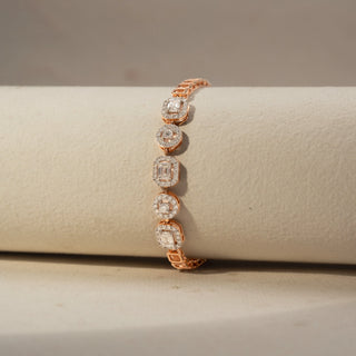 Close up view of a diamond station bracelet in 14 KT Rose Gold, featuring alternating round and emerald-cut lab-grown diamonds in elevated halo settings, displayed on a beige surface.