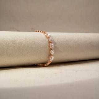Side view of a diamond station bracelet in 14 KT Rose Gold, featuring alternating round and emerald-cut lab-grown diamonds in elevated halo settings, gracefully displayed on a beige surface.