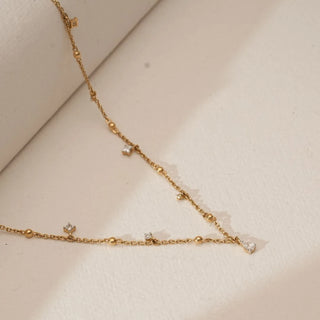 Top view of yellow gold station necklace with polished bead accents and dangling pear-shaped lab grown diamond drops arranged along a fine chain on a soft neutral surface.