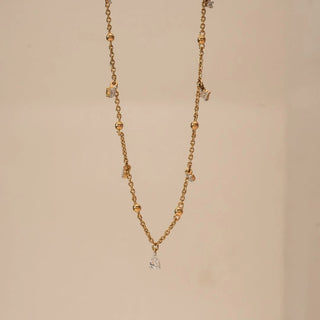 Front view of yellow gold station necklace featuring polished bead accents and dangling pear-shaped lab grown diamond drops, centred with a larger pear diamond pendant on a neutral backdrop.