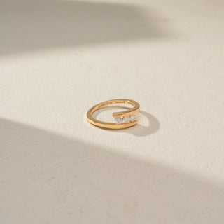 Top view of a minimalist open-band yellow gold ring featuring three round diamonds nestled between sleek parallel ends, displayed on a neutral surface in soft natural light.