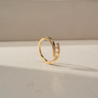 Angled side view of a yellow gold open-wrap ring featuring three round diamonds set between overlapping bands, displayed on a neutral surface in soft natural light.