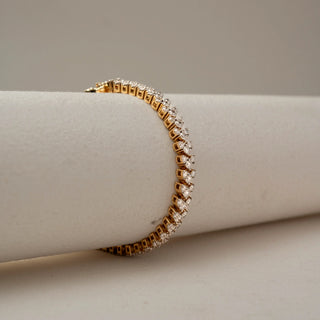 Side view of a gold bracelet with alternating heart-shaped and round brilliant gemstones in raised settings, elegantly wrapped around a soft neutral display stand.