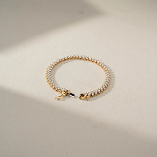 Top view of a classic gold tennis bracelet featuring a continuous row of round brilliant gemstones and a secure clasp, displayed on a soft neutral background.