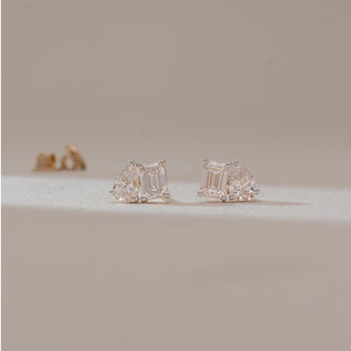 Front view of diamond stud earrings in white gold, featuring emerald-cut lab-grown diamonds paired with pear-shaped side stones. Captured against a soft beige background with subtle shadows.
