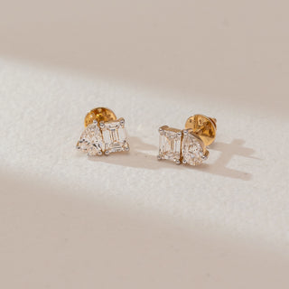 Angled view of diamond stud earrings in white gold, featuring emerald-cut lab-grown diamonds paired with pear-shaped side stones. Set against a soft beige textured background with gentle shadows.