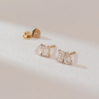 Side angled view of diamond stud earrings in white gold, featuring emerald-cut lab-grown diamonds paired with pear-shaped side stones. Captured against a soft beige textured background.