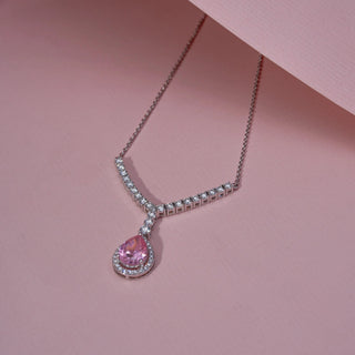 Angled view of a pink gemstone and lab-grown diamond pendant necklace in 14KT White Gold, featuring a pear-shaped pink centre stone with a diamond halo. Captured against a pink backdrop, the elegant design radiates brilliance.