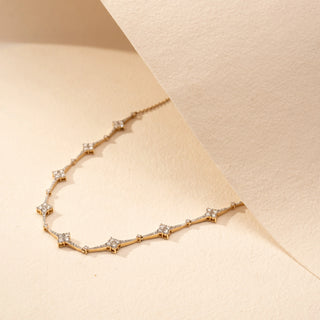 Angled view of a star-inspired lab-grown diamond necklace in 14KT Yellow Gold, featuring bezel-set diamond star motifs linked by a delicate chain. Captured against a beige backdrop, the elegant design radiates subtle brilliance.
