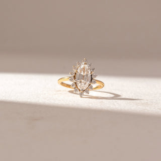 Front view of Marquise Halo Diamond Ring in 14KT Yellow Gold, featuring a marquise-cut center diamond encircled by round halo diamonds. Set on a soft beige surface, the design radiates classic elegance and sparkle.
