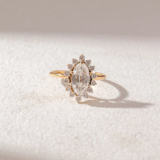 Top view of Marquise Halo Diamond Ring in 14KT Yellow Gold, featuring a marquise-cut center diamond surrounded by petal-shaped halo diamonds. Set on a soft beige surface, it reflects timeless elegance and sparkle.
