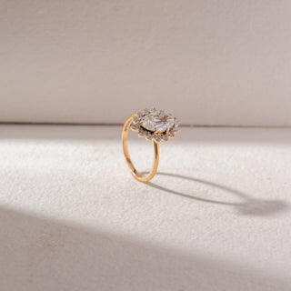 Angled side view of Marquise Halo Diamond Ring in 14KT Yellow Gold, featuring a marquise-cut center diamond with petal-shaped halo accents. Set on a beige surface, it reflects delicate brilliance and elegance.
