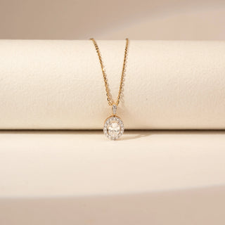Close up view of a 14KT Yellow Gold diamond pendant with an oval centre diamond, diamond-set halo and a diamond-set bail.