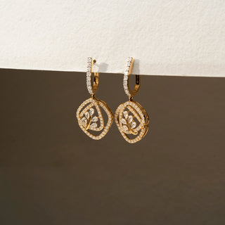 Angled view of geometric diamond drop earrings in 14 KT Yellow Gold, featuring pavé-set circular frames with leaf-inspired diamond motifs against a neutral backdrop.
