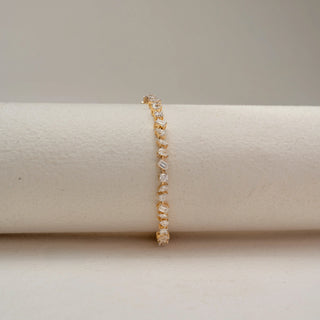 Front view of a mixed-shape diamond tennis bracelet in 14 KT Dual Gold, featuring alternating emerald-cut, pear-shaped, and round lab-grown diamonds, displayed on a beige surface.
