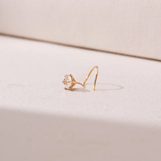 Side view of a yellow gold nose pin, featuring a solitaire round diamond in a minimal prong setting. Captured against a soft beige backdrop, the design reflects delicate sparkle and understated elegance.