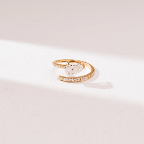 Front angle view of a 14KT yellow gold pear solitaire bypass diamond ring with a prong-set pear-shaped center stone and a curved pavé diamond band in an open wrap design.