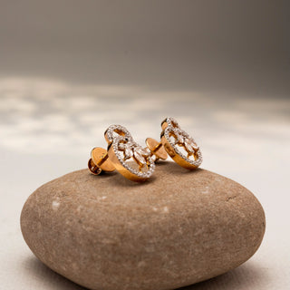 Side view of floral diamond stud earrings in 14 KT Yellow Gold, featuring pavé-set circular motifs with marquise diamond petals, displayed on a textured stone surface.