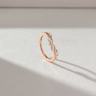 Side profile of curved diamond ring in rose gold, featuring marquise-shaped lab-grown diamonds set along a flowing wave band. Captured against a soft beige textured background with gentle shadows.