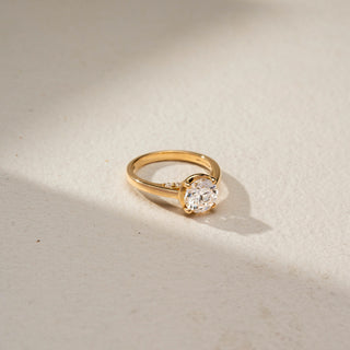 Top view of a round solitaire engagement ring in 14 KT Yellow Gold, featuring a round lab-grown diamond in a classic four-prong setting on a sleek polished band, displayed against a beige backdrop.