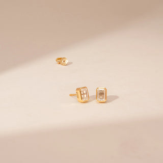 Angled view of 14KT Yellow Gold diamond earrings, featuring rectangular step-cut diamonds in bezel settings.