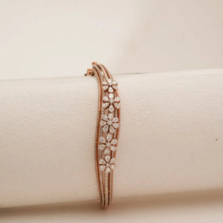 Front view of rose gold floral diamond bangle featuring layered blossom motifs with pear-shaped petal diamonds and round centres, set on a triple-band frame against a soft neutral backdrop.