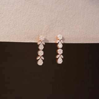 Close up view of diamond drop earrings in 14 KT Yellow Gold, featuring cascading round and pear-shaped diamond clusters with marquise accents against a neutral backdrop.
