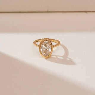 Top view of Modern Bezel Solitaire Diamond Ring in yellow gold, featuring an oval lab-grown diamond enclosed in a sleek bezel setting, displayed on a soft beige backdrop.