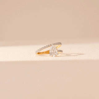 Front view of a 14KT yellow gold ring featuring a pear-cut diamond and round diamonds, set against a beige background.
