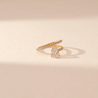 Close-up view of a 14KT yellow gold ring featuring a pear-cut diamond and round diamonds, set against a beige background.