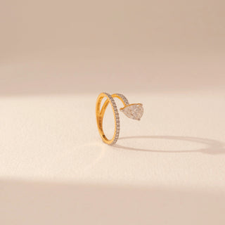 Angled view of a 14KT yellow gold ring featuring a pear-cut diamond and round diamonds, set against a beige background.