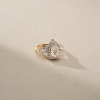 Top view of a pear halo engagement ring in 14 KT Yellow Gold, featuring a pear-shaped lab-grown diamond encircled by a double halo and accented by pear-shaped side diamonds, displayed against a beige backdrop.