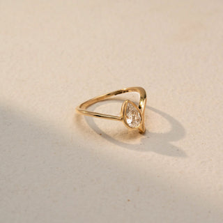 Side view of a pear solitaire ring in 14 KT Yellow Gold, featuring a pear-shaped lab-grown diamond nestled within a sleek sculpted bypass setting, displayed against a beige backdrop.