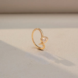 Angled view of a pear solitaire ring in 14 KT Yellow Gold, featuring a pear-shaped lab-grown diamond nestled within a sleek sculpted bypass setting, displayed against a beige backdrop.