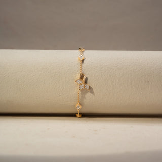 Front view of a geometric diamond bracelet in 14 KT Yellow Gold, featuring open kite-shaped motifs accented with clustered diamonds and delicate chain links, displayed against a soft beige backdrop.
