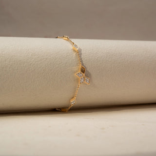 Side view of a geometric diamond bracelet in 14 KT Yellow Gold, featuring open kite-shaped motifs accented with clustered diamonds and delicate chain links, displayed against a soft beige backdrop.
