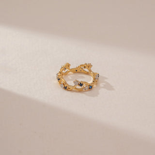 Top view of a blue sapphire and diamond ring in 14KT Yellow Gold, featuring an intertwined vine band against a beige backdrop.