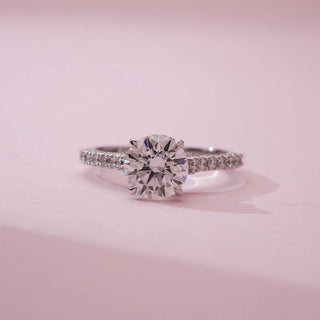 Front close view of Elegant Pavé Shank Diamond Ring in white gold, featuring a round lab-grown centre diamond with pavé-set round diamonds along the slender band, displayed on a soft pink background.