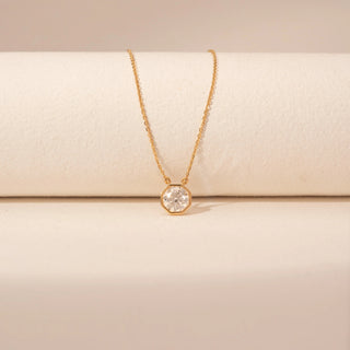 Close-up view of a 14KT yellow gold necklace featuring a round-cut diamond pendant, set against a beige background.